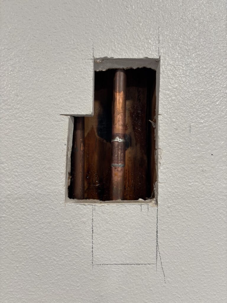 Copper water pipe and fitting visible through a wall access opening